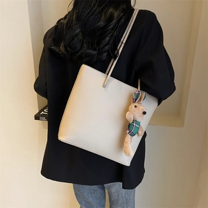 Minimalist beige leather tote bag with rabbit charm shown on model in black suit