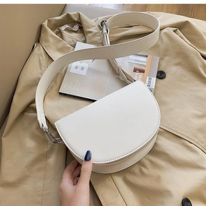 Flat lay of a white leather saddle bag on a trench coat with a wide adjustable strap