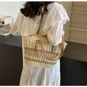 Close-up of a large woven straw tote bag with brown leather handles worn over a white dress