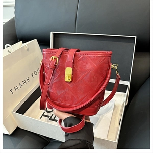 Detail of red geometric textured bucket bag featuring a gold twist lock and shoulder strap