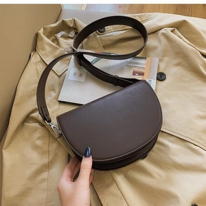 Detail view of a dark brown crescent saddle bag with wide strap and silver metal buckle