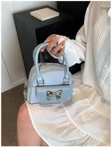 Detail of light blue bucket bag featuring a silver metal bow accent and pebble texture