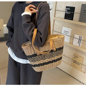 Detail of woven straw tote bag featuring black stripes and brown leather handles