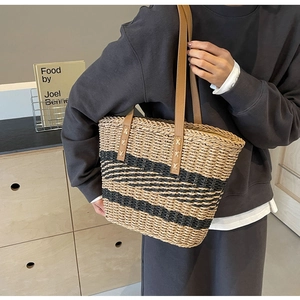 Detail of hand-woven straw tote with black stripes and brown leather straps for travel