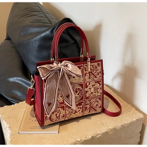 Detailed close-up of red leather handbag featuring exquisite gold floral embroidery and scarf
