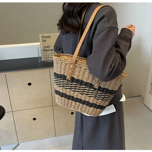 Detail of handwoven straw tote with black stripes and brown leather straps reinforced by X-stitching