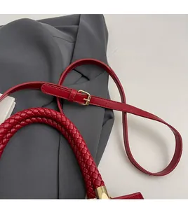 Detail of red leather shoulder strap with golden buckle and woven handle on the handbag