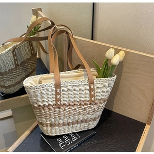 Detail of striped straw tote bag featuring brown leather straps and cross-stitch accents