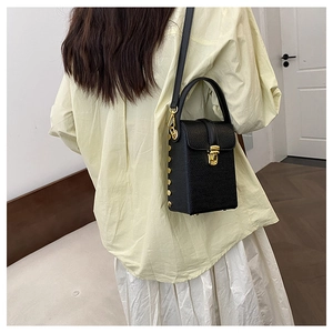 Detail of black woven box bag with gold lock and studs worn cross-body with casual outfit