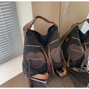 Detail showing black canvas tote bag with brown heart zipper pockets and long leather tassels