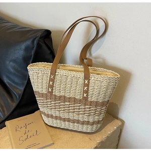 Close-up of woven straw tote bag with brown leather handles and decorative stitching