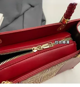 Detail of red wedding bag with gold embroidery, smooth zipper and woven handle