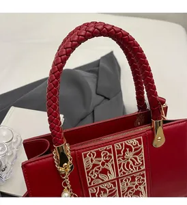 Detail of red bridal handbag featuring golden floral embroidery and pearl chain accessory