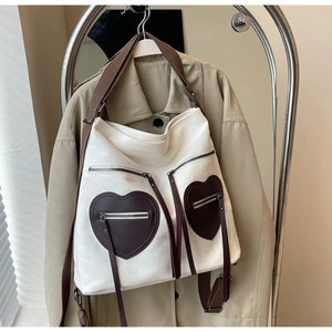 Detail of canvas tote bag featuring brown heart-shaped pockets and elegant long tassels