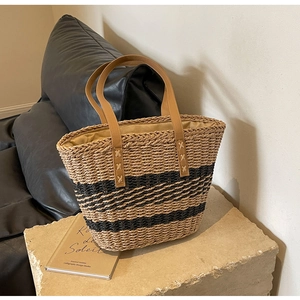 Detail of hand-woven straw tote bag with black stripes and brown leather handle