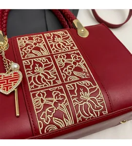 Detail of red wedding handbag with golden floral embroidery and pearl heart charm