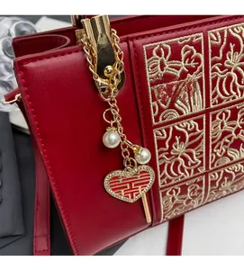 Detail of red wedding handbag with golden floral embroidery and pearl heart pendant