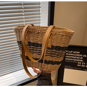 Close-up of woven straw beach bag featuring black stripes and brown faux leather handles