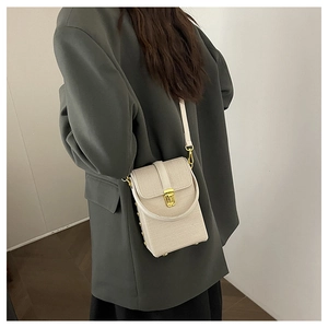 Close-up of cream vertical mini mobile phone bag worn by a model in a dark blazer