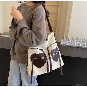 Detail of canvas tote bag featuring heart-shaped zipper pockets and long fringe tassels