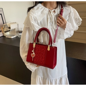 Detail of red wedding handbag with floral embossing and heart-shaped Xi charm on handle