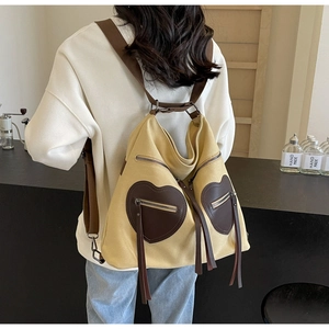 Detail of yellow canvas backpack showing brown heart patches and leather tassels