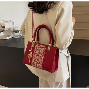 Detail of red bridal handbag with golden floral embroidery and pearl heart charm