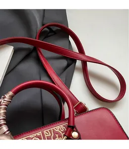 Detail of red leather wedding bag with silk scarf handle and golden vintage embossed pattern