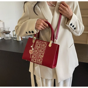 Close-up of red wedding handbag featuring gold floral embroidery and heart pearl pendant