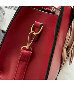 Close-up of red textured leather handbag featuring golden metal hooks and silk scarf detail
