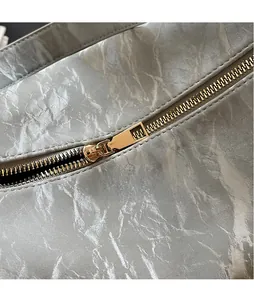 Close-up of golden zipper hardware on high-texture off-white pleated leather dumpling bag