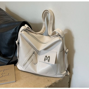 Detailansicht der cremeweißen Tragetasche mit silbernem M-Logo und mehreren Taschen