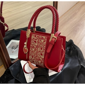 Detail of red wedding handbag featuring gold floral embroidery and heart pearl charm