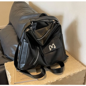 Detail eines schwarzen Lederrucksacks mit silbernem M-Logo und mehreren Reißverschlüssen