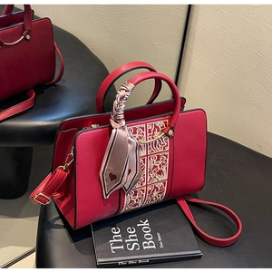 Macro detail of red PU leather bag featuring floral embroidery and silk scarf handle