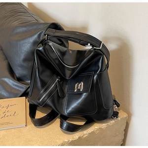 Detail eines schwarzen Lederrucksacks mit silbernem M-Logo und mehreren Reißverschlüssen