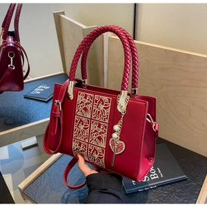 Detail of red bridal handbag featuring golden floral embroidery and pearl heart charm