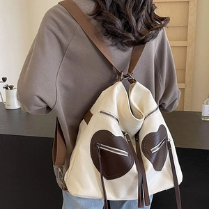 Off-white canvas backpack with brown heart-shaped leather pockets and fringe zippers