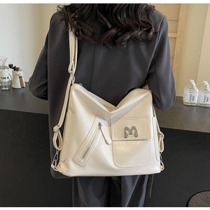 Detail der cremeweißen Kunstledertasche mit mehreren Taschen und modischem M-Logo-Detail