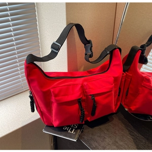 Detail of red nylon messenger bag featuring utility pockets and adjustable black strap