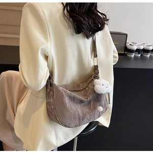 Detailed texture of a grey pleated crescent bag with a cute white plush cloud charm