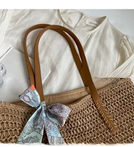 Close-up of woven straw tote bag with brown leather handles and decorative floral silk scarf