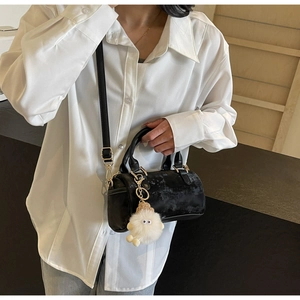 Detail of a black velvet Boston bag with gold hardware and white plush keychain charm