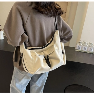 Detail of cream canvas crossbody bag showing dual front pockets and utility style zippers