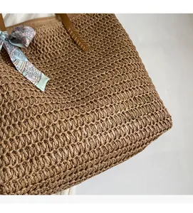 Detail of woven straw tote bag with floral silk scarf and brown leather handle stitching