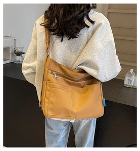 Detail of caramel tote bag with multiple pockets and blue label on a person