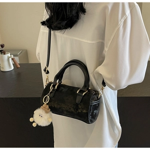 Detail of black Boston bag with gold hardware and plush charm on adjustable strap