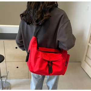 Model wearing a large red canvas crossbody tote bag with adjustable black strap