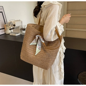 Detail of woven straw tote bag with leather straps and blue floral silk scarf accent