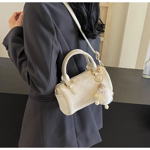 Detail of a beige Boston bag with gold-tone hardware and a plush monster charm